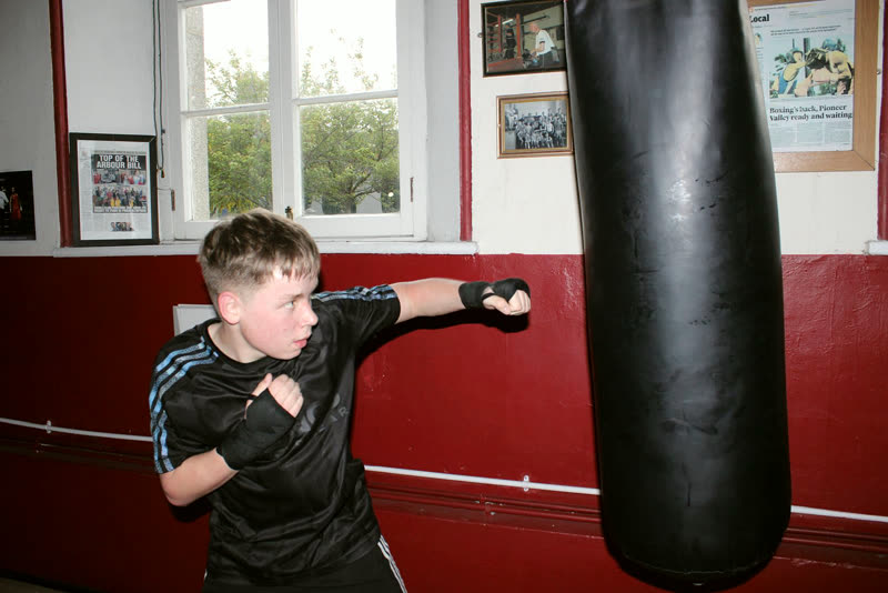 A boy working the heavy bag, framed newspaper cuttings on the wall behind him