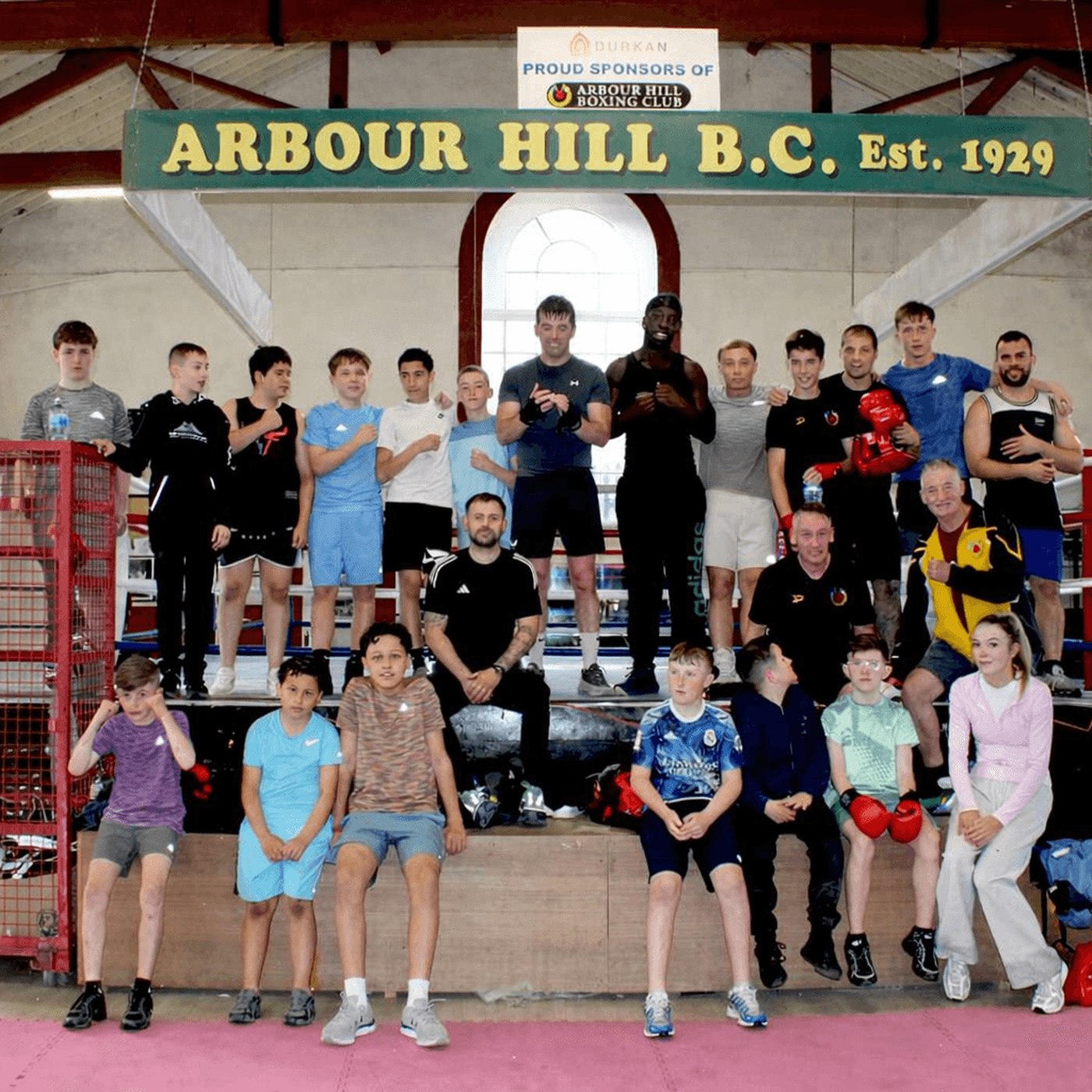 The whole Arbour Hill club in the ring under the Est. 1929 sign: children seated in front, teenagers and coaches behind