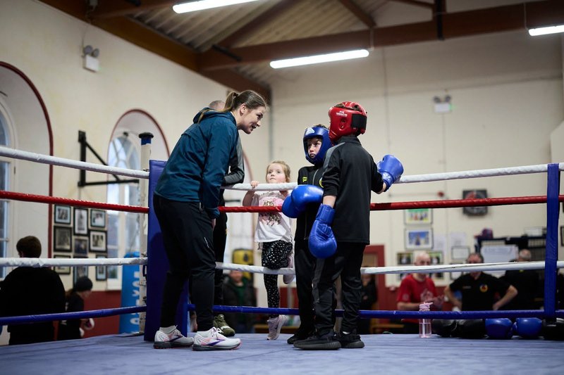 A coach talking to two young boxers in headgear inside the ring