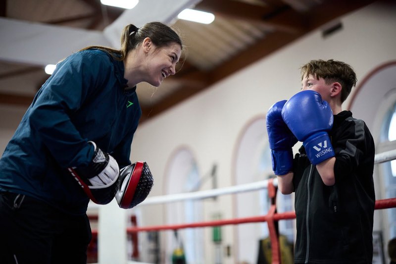 A coach holding pads for a young boxer in the club ring