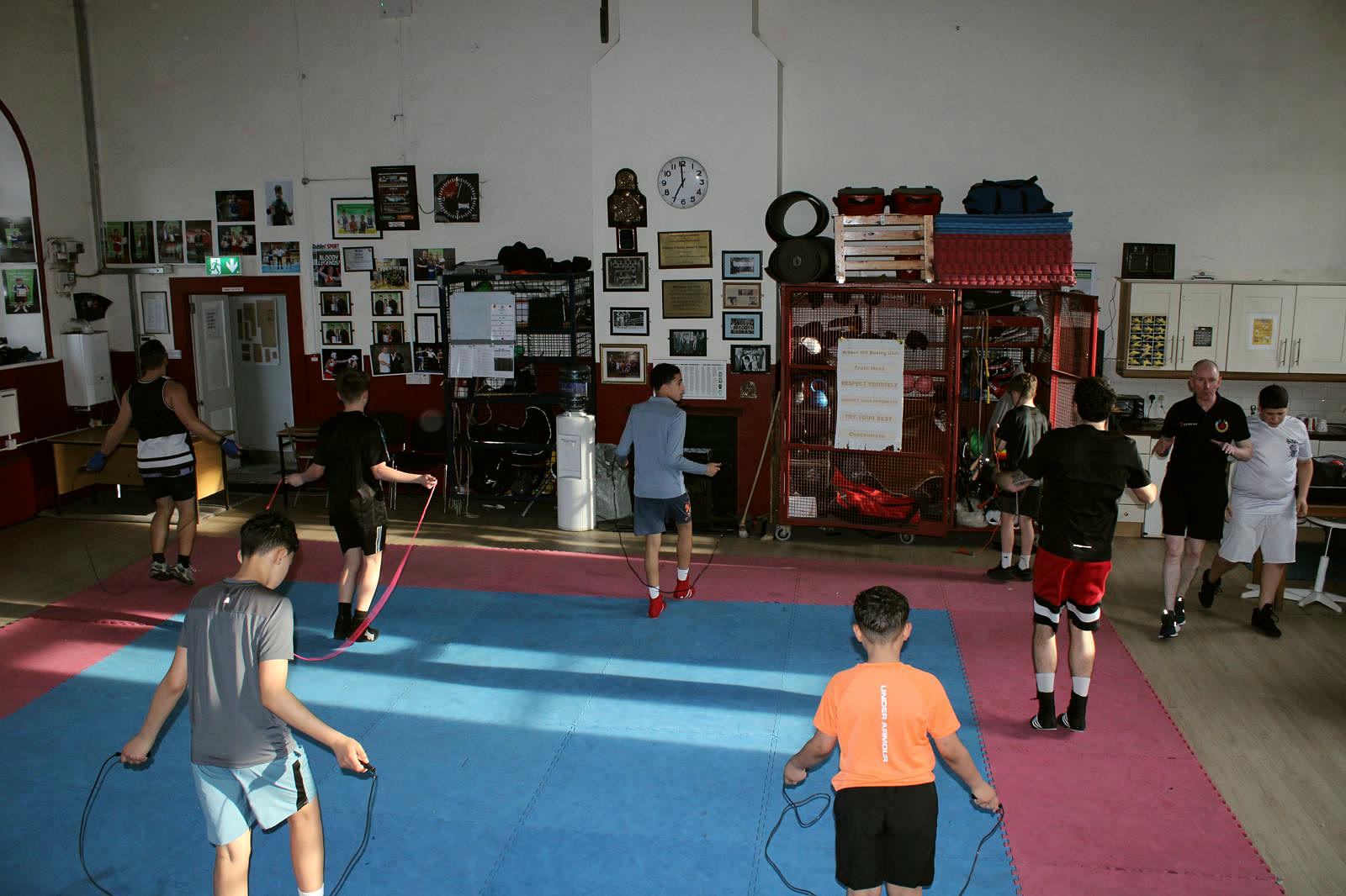 The Arbour Hill hall on a training night: boys skipping on the mats, the back wall covered in framed photographs and plaques