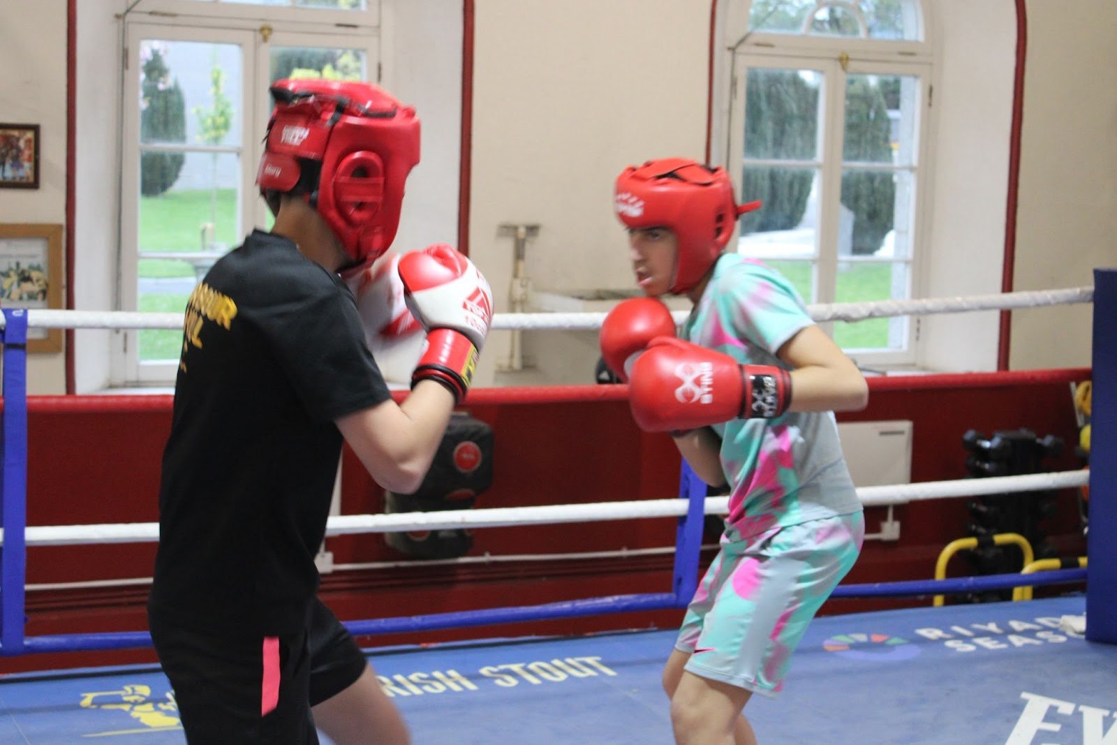 Two young boxers in red headgear and gloves working in the ring at Arbour Hill, guards up